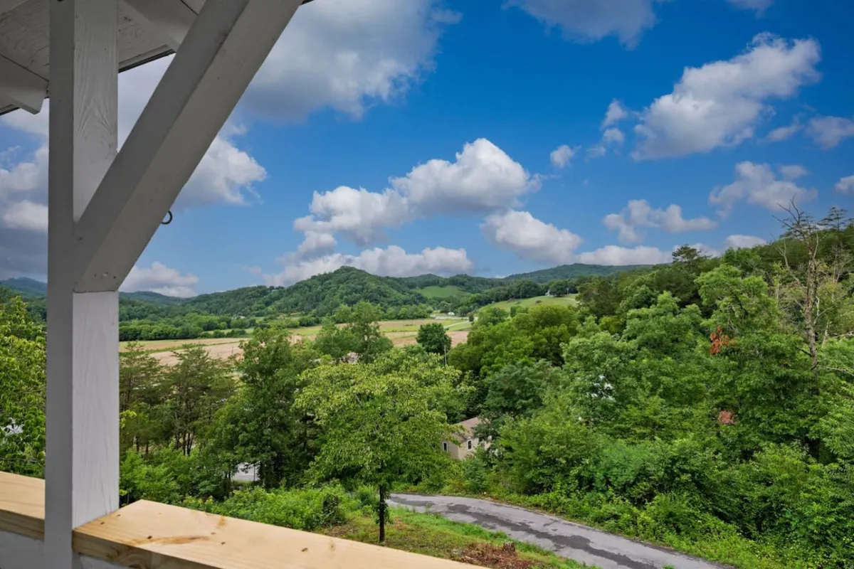A panoramic view of a mountain range framed by lush greenery and a winding road, under a cloudy sky. The landscape evokes a sense of exploration and natural beauty just beyond the property.
