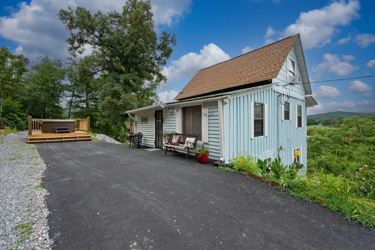 This image shows the charming blue house with its spacious wooden deck and lush greenery all around. The deck is an ideal space for relaxing, watching the sunset, or letting pets enjoy the fresh mountain air.