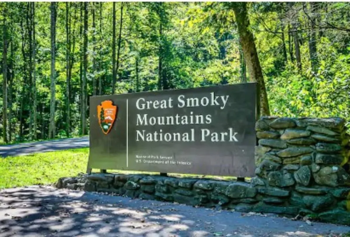 This image features the iconic Welcome sign to Great Smoky Mountains National Park, set against natural surroundings with a stone wall and lush greenery. The scene immediately places viewers at the gateway to adventure, evoking the excitement of exploration.