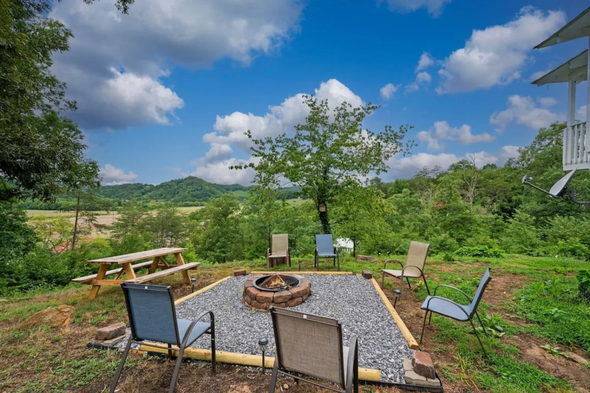 A cozy fire pit area with surrounding chairs and a picnic table, nestled within a lush landscape. The setting is perfect for campfire gatherings, storytelling, and late-night s’mores sessions under the stars.