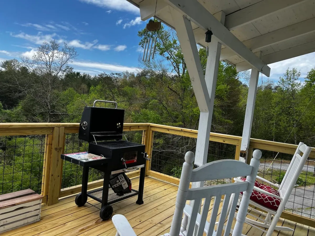 This image features an inviting wooden deck with rocking chairs, a grill, and a panoramic scenic view stretching into the distance. The tranquil outdoor setting is perfect for couples, with space for relaxing together, shared meals, and enjoying nature. The warm light suggests the ideal environment for sunset watching and stargazing.