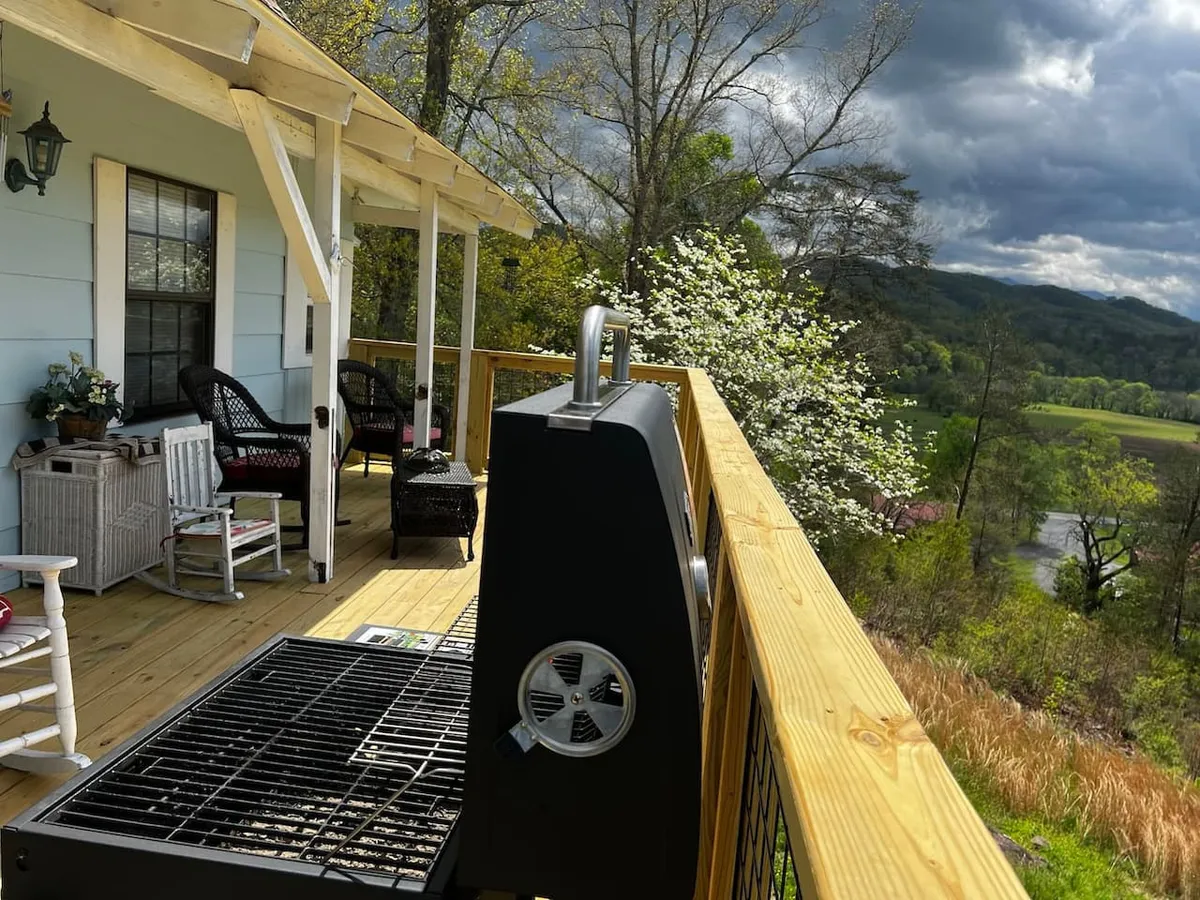 This image showcases an exterior deck with a grill, multiple rocking chairs, potted plants, and views of the surrounding wooded area. The setting exudes a casual, welcoming mood, perfect for family gatherings, barbecues, or simply relaxing while enjoying the outdoors.