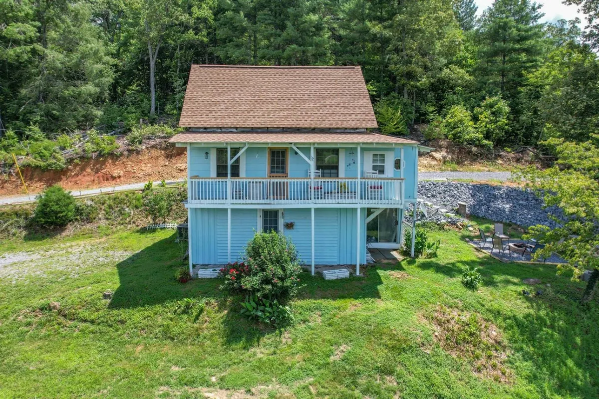 This image showcases the blue exterior of the house with its inviting balcony, surrounded by lush greenery. The balcony is furnished to encourage outdoor relaxation, and the setting radiates tranquility, with ample opportunities to enjoy sunsets, morning coffee, or peaceful evenings.