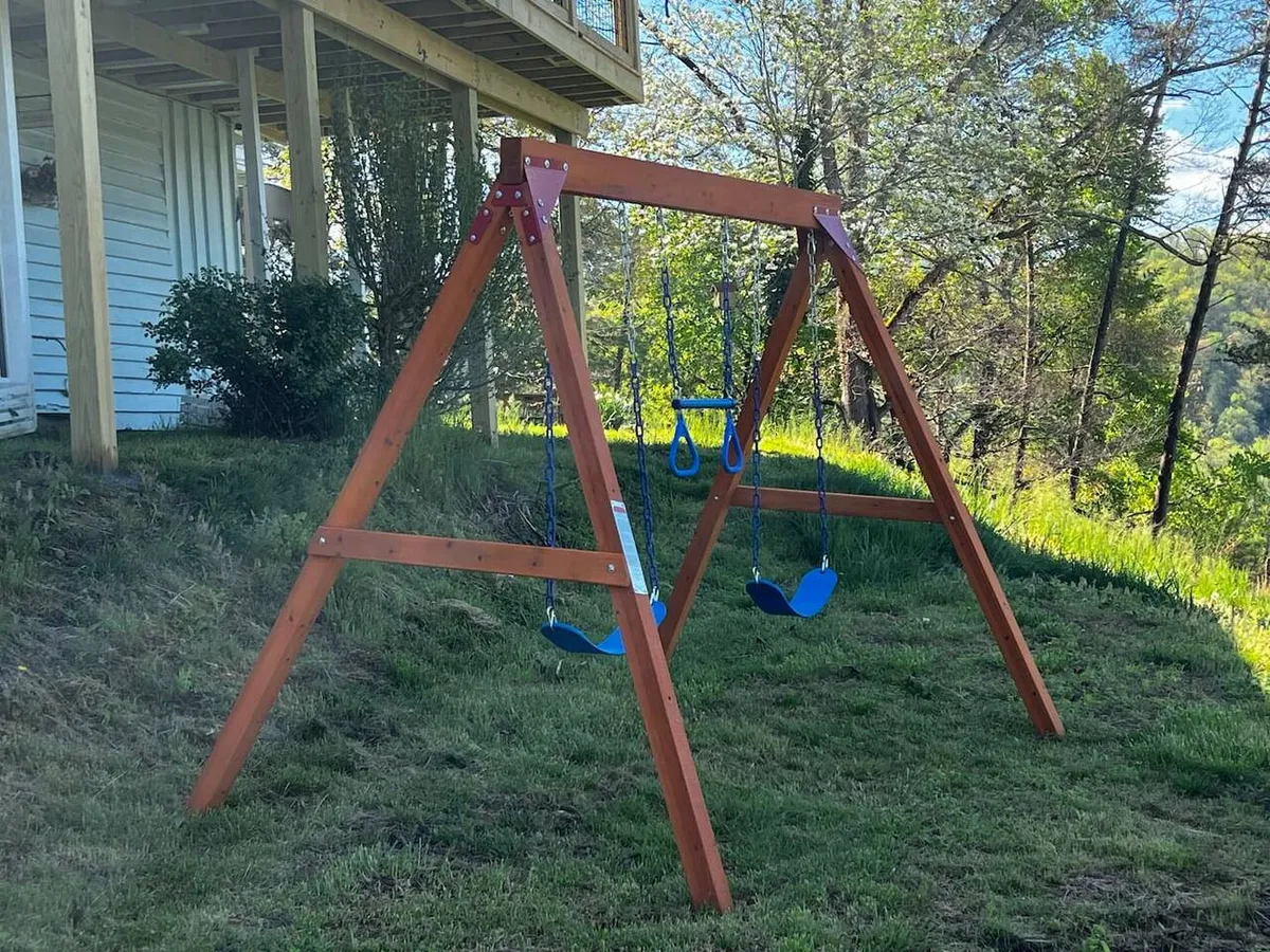 A joyful outdoor scene with a wooden swing set, lush green grass, and surrounding trees, inviting children to play and families to gather for picnics or celebrations in the fresh air.