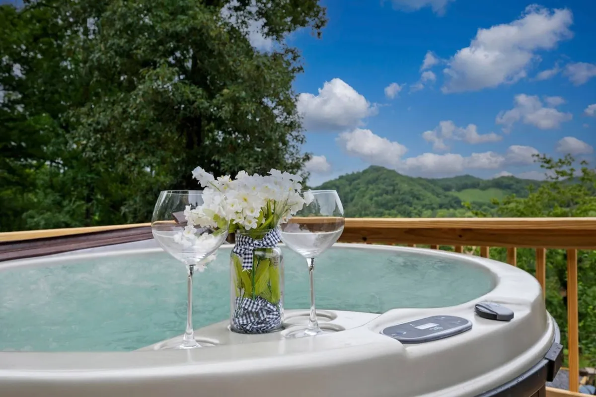 A scenic hot tub set on a deck, surrounded by flowers and offering a breathtaking mountain view. Glasses of champagne suggest a romantic or celebratory atmosphere, ideal for unwinding after a day outdoors.
